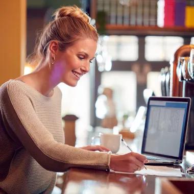 Woman writing notes at bar counter with laptop open