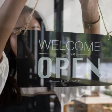 Woman hanging 'Welcome, please come in' door sign