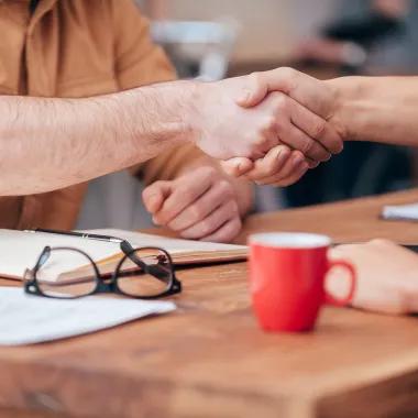 Two shaking hands on a table with notes
