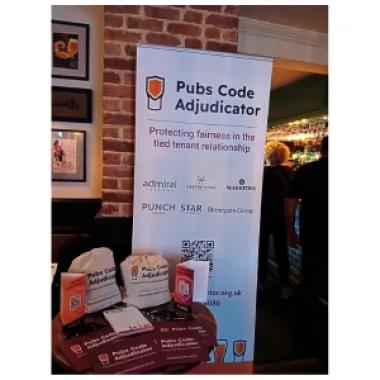 Corner set-up with Pubs Code merch on a table and our banner
