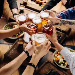 A group of people cheersing beer glasses with lots of food surrounding them