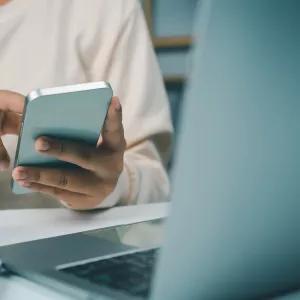 A person scrolling on phone with laptop also on the screen. Looking for information